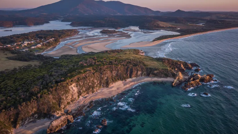 Aerial view of a rocky headland and curving beach, with Gulaga rising behind