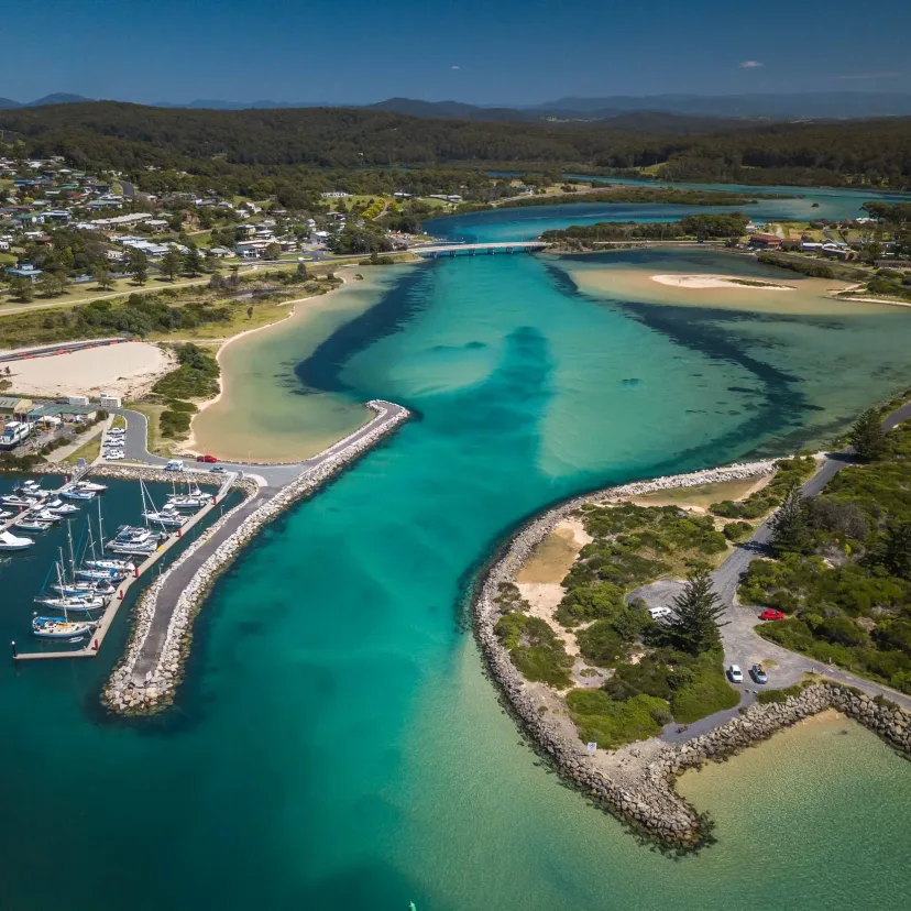 Aerial view of Bermagui marina and breakwater, with moored boats and the turquoise river mouth