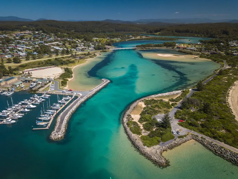 Aerial view of Bermagui marina and breakwater, with moored boats and the turquoise river mouth