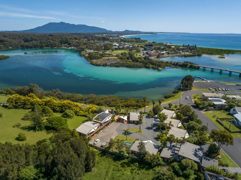 Aerial view of The Anchorage beside the Bermagui River, with the bridge and mountains behind