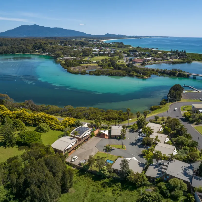 Aerial view of The Anchorage beside the Bermagui River, with the bridge and mountains behind
