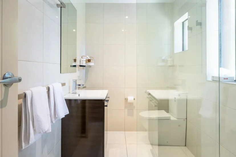 Apartment bathroom with a glass shower, basin and folded white towels