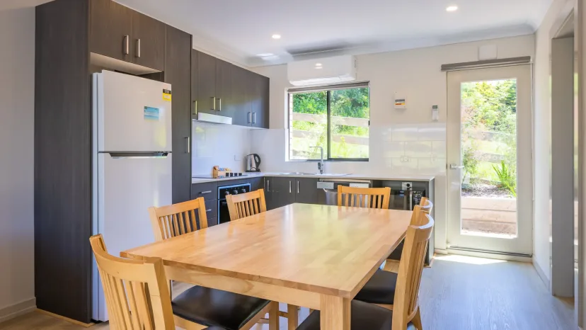 Apartment kitchen and dining area with a timber table and a door out to the garden