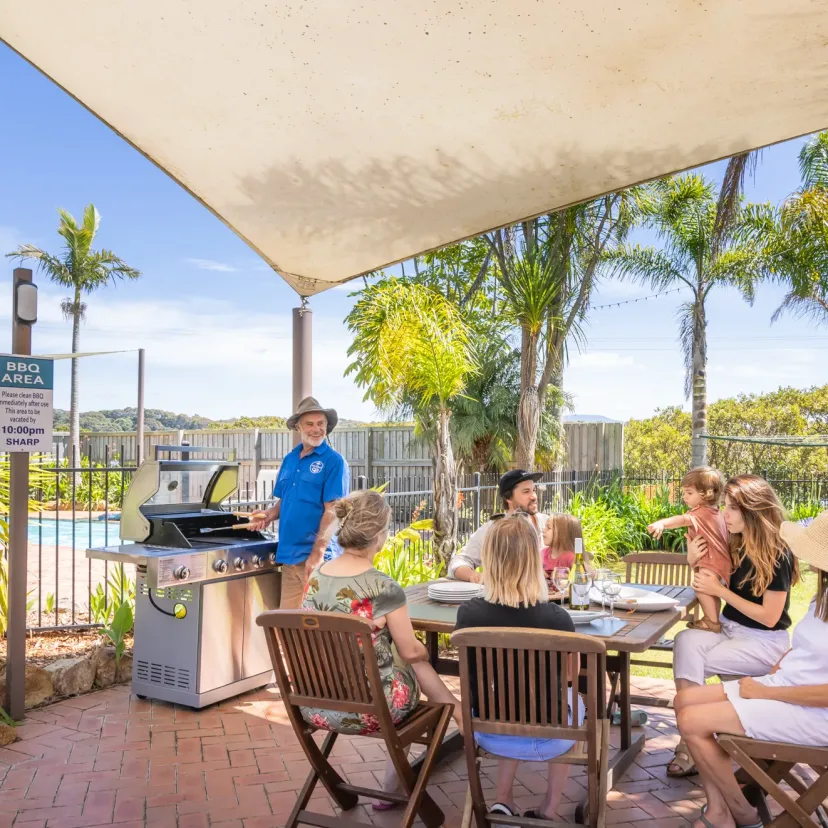 Guests eating together under the sail shade in the communal BBQ area beside the pool