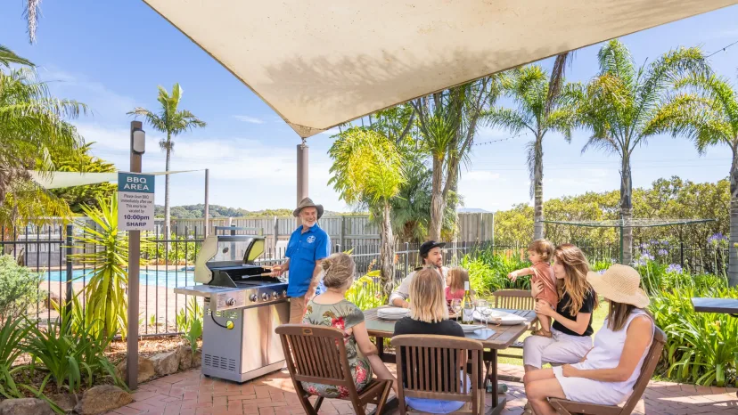 Guests eating together under the sail shade in the communal BBQ area beside the pool