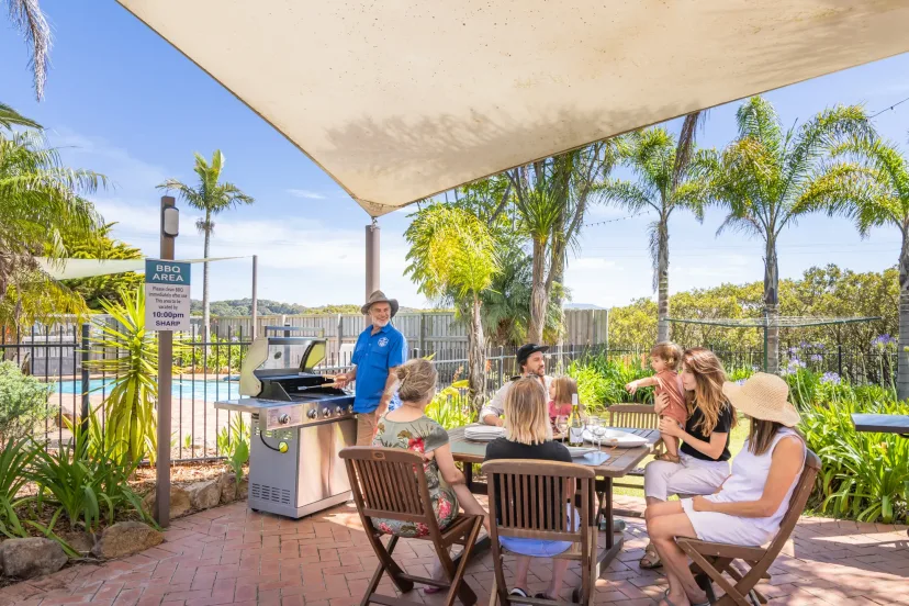 Guests eating together under the sail shade in the communal BBQ area beside the pool