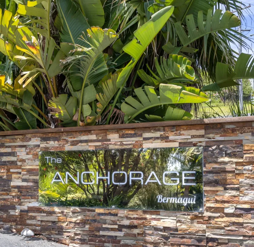 The Anchorage Bermagui entrance sign, a glass panel on a stacked stone wall below tropical palms