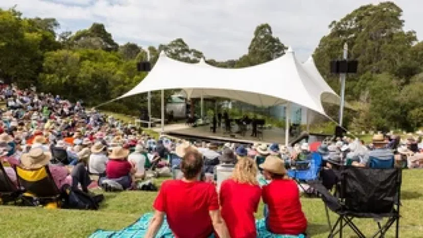 A crowd sitting on the grass in front of the Four Winds shell stage at Barragga Bay
