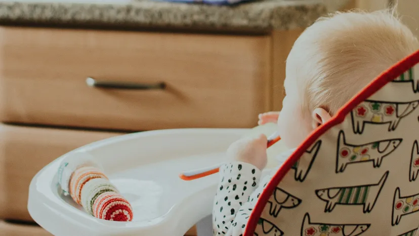 A baby in a high chair at the kitchen bench, with a toy on the tray in front of them