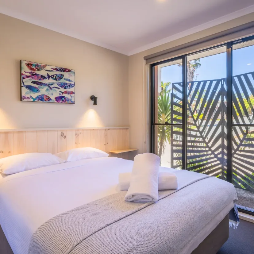 Bright bedroom with crisp white linen, fish artwork and a screened balcony
