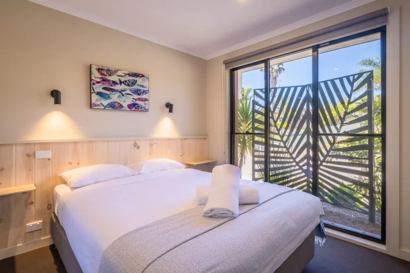 Bright bedroom with crisp white linen, fish artwork and a screened balcony