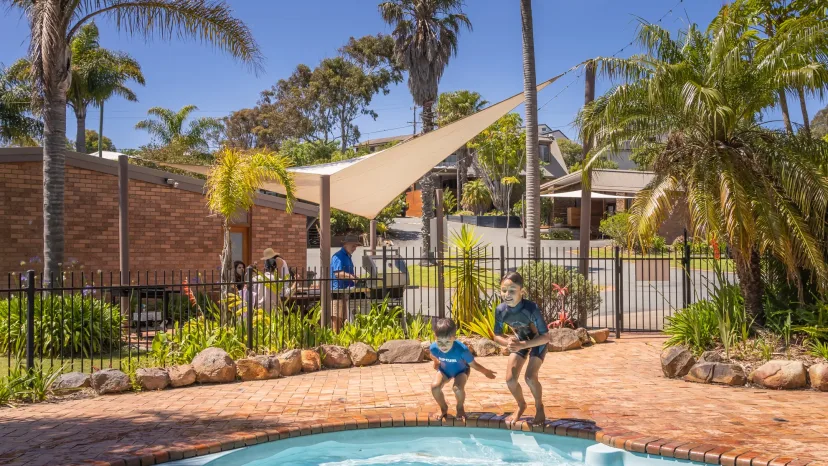 Children jumping into the swimming pool under the sail shade