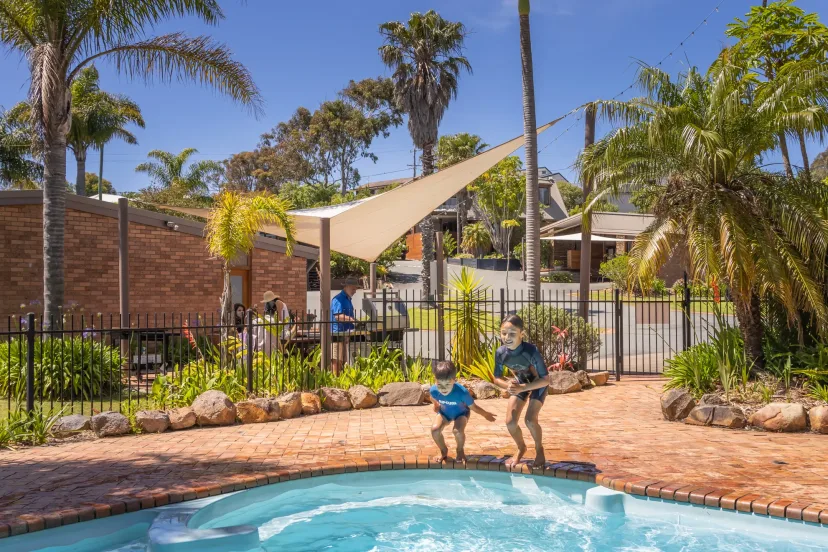 Children jumping into the swimming pool under the sail shade