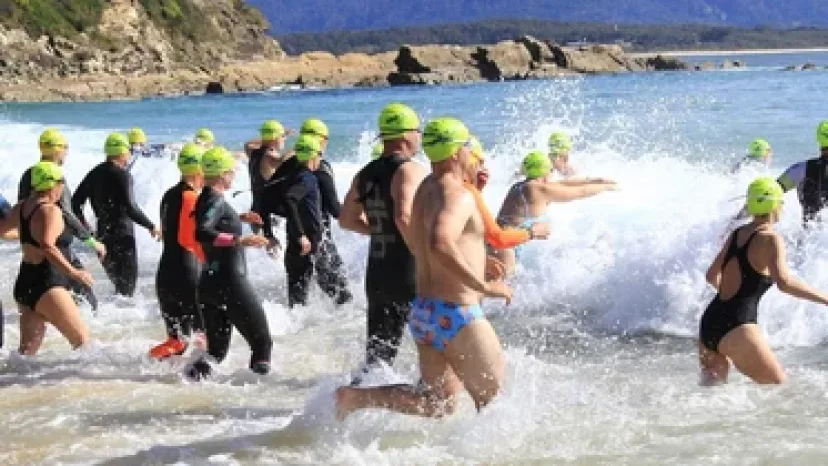 Swimmers in green caps running into the surf at the start of the Reboot Bermagui ocean swim