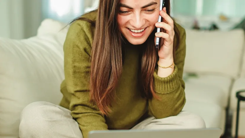 A guest sitting on a lounge with a laptop open in front of her, smiling while she talks on her phone